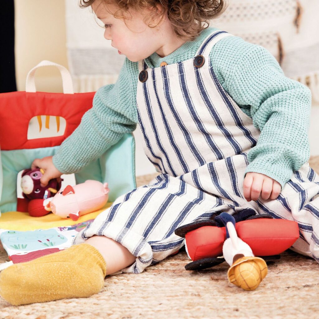 Niño jugando con una granja de peluche, juego simbólico infantil